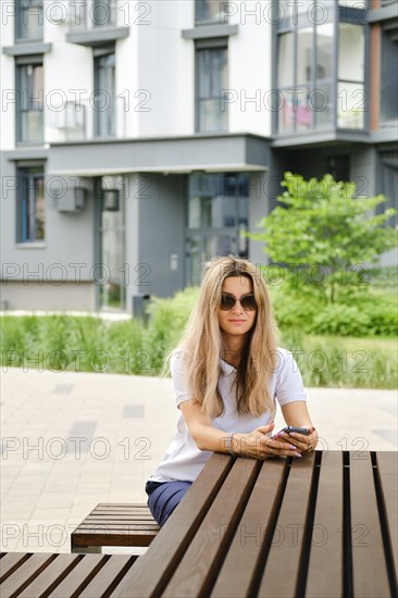 Woman called taxi using mobile application and is waiting for car while sitting on bench