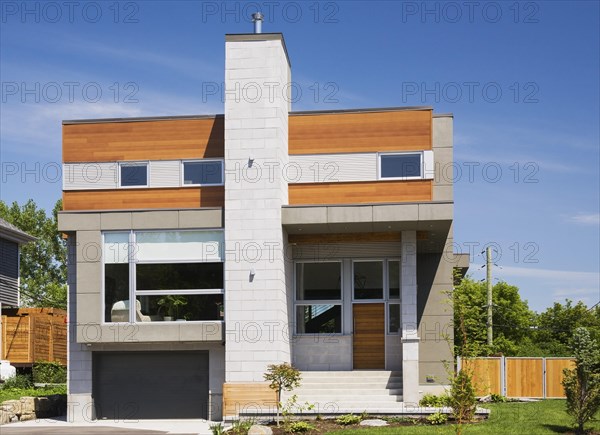 Two story grey and charcoal stone with cedar wood siding modern cube style home facade in summer, Quebec, Canada, North America