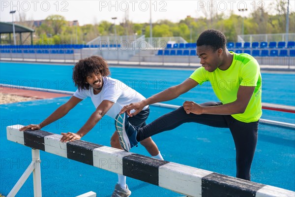 Two young african american sportsmen talking distracted while stretching legs in a running track