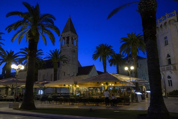 Outdoor restaurant at night with historic church tower and palm trees, Trogir, Dalmatia, Croatia, Europe