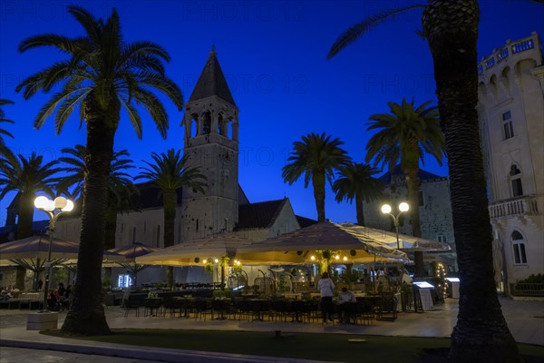 Outdoor restaurant at night with historic church tower and palm trees, Trogir, Dalmatia, Croatia, Europe