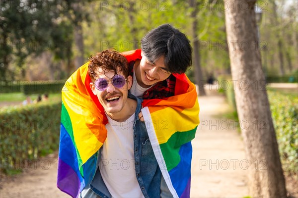 Multi-ethnic gay men wrapping in lgbt flag piggybacking in a park