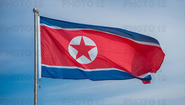 The flag of North Korea flutters in the wind, isolated against a blue sky