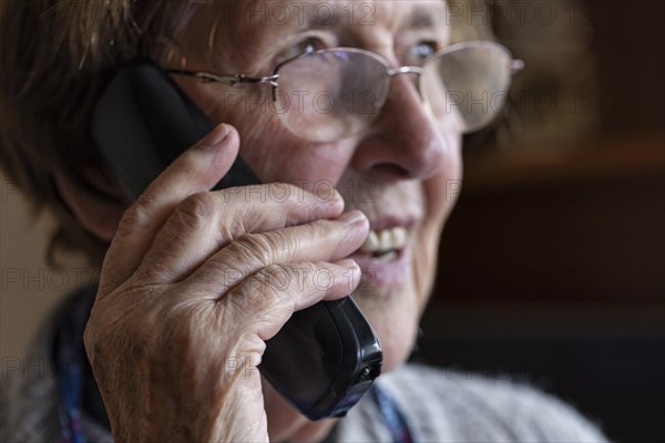 Laughing senior citizen with smock talking on the phone at home in her living room, Cologne, North Rhine-Westphalia, Germany, Europe