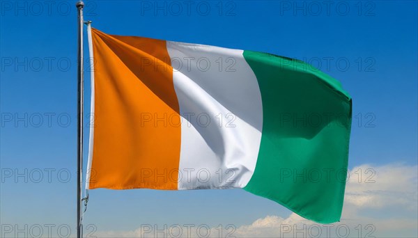 The flag of Ivory Coast flutters in the wind, isolated, against the blue sky