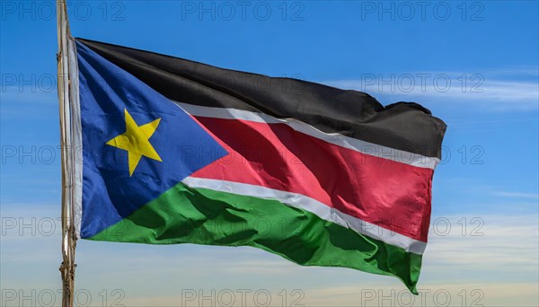 The flag of South Sudan, fluttering in the wind, isolated, against the blue sky