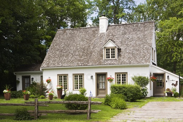 Old circa 1886 white with beige and brown trim Canadiana cottage style home facade in summer, Quebec, Canada, North America