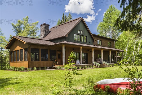 Rear view of brown and green stained spruce wood and cedar shingle siding LEED certified Country home with veranda in late spring, Quebec, Canada, North America