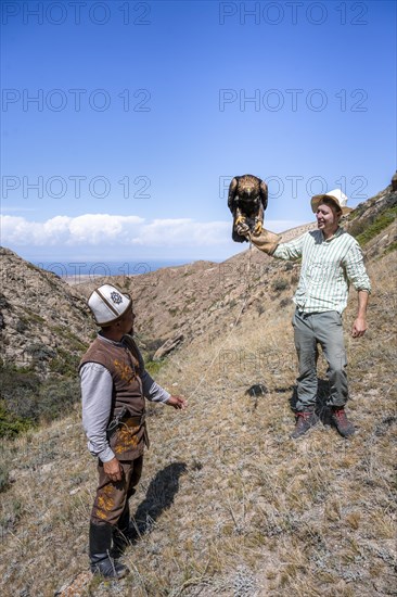 Traditional Kyrgyz eagle hunter, tourist holding eagle in his arms, near Bokonbayevo, Issyk Kul region, Kyrgyzstan, Asia