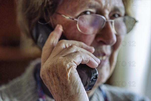 Laughing senior citizen talking on the phone at home in her living room, Cologne, North Rhine-Westphalia, Germany, Europe