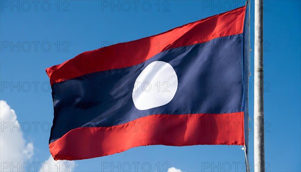 The flag of Laos flutters in the wind, isolated against a blue sky