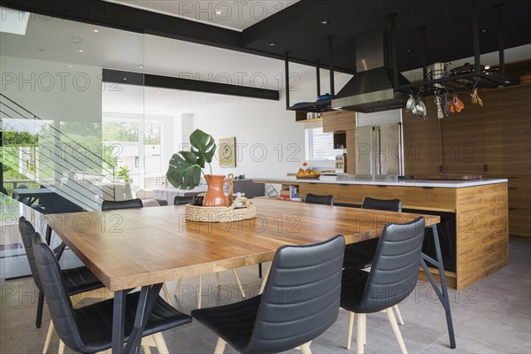 American walnut wood dining table and black leather sitting chairs with ash wood legs in dining room kitchen area inside modern cube style home, Quebec, Canada, North America