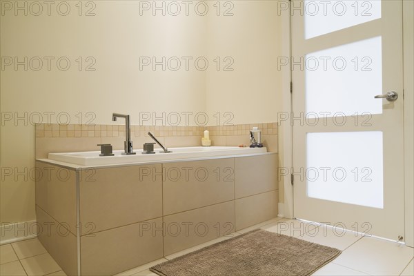 Soaking tub encased in a ceramic tile base in bathroom inside a renovated ground floor apartment in an old residential cottage style home, Quebec, Canada, North America