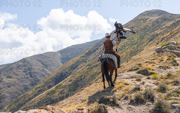 Traditional Kyrgyz eagle hunter riding with eagle in the mountains, hunting on horseback, near Bokonbayevo, Issyk Kul region, Kyrgyzstan, Asia