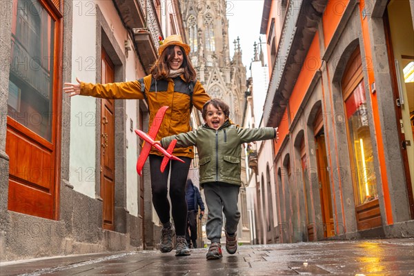 A woman and a child are playing with a red kite in a narrow alleyway. The scene is lively and playful, with the two of them enjoying their time together