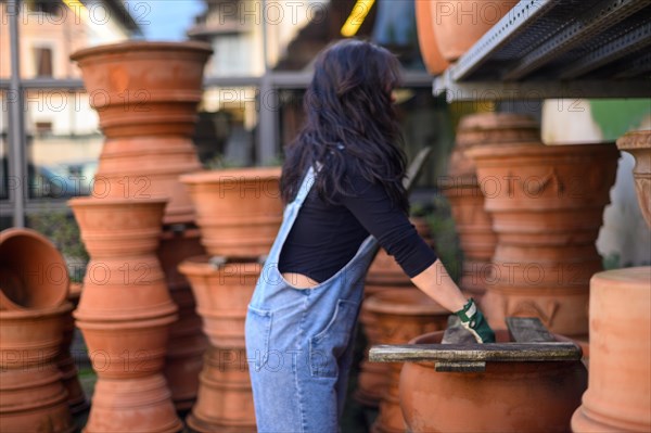 Back view of a woman in a pottery workshop surrounded by terracotta pots