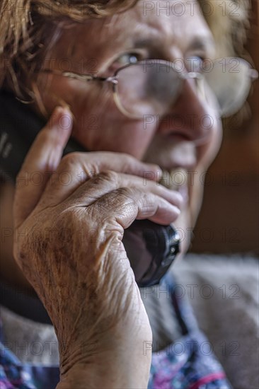 Laughing senior citizen with smock talking on the phone at home in her living room, Cologne, North Rhine-Westphalia, Germany, Europe