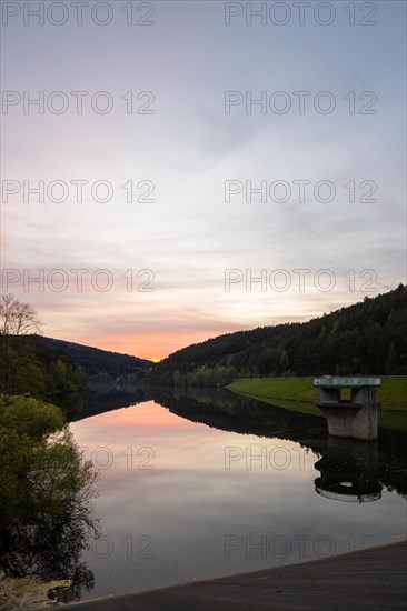 A lake in a landscape shot. A sunset and the natural surroundings are reflected in the water of the reservoir. Marbach reservoir, Odenwald, Hesse