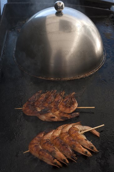 Spit-roasted prawns on a plancha, gas grill, stainless steel cooking bell in the back, Vandee, France, Europe