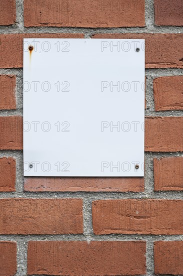 Blank white notice board attached to a brick wall with four screws, background with Copyspace