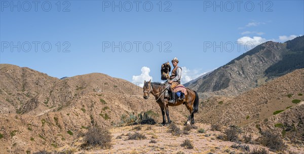 Traditional Kyrgyz eagle hunter riding with eagle in the mountains, hunting on horseback, near Bokonbayevo, Issyk Kul region, Kyrgyzstan, Asia