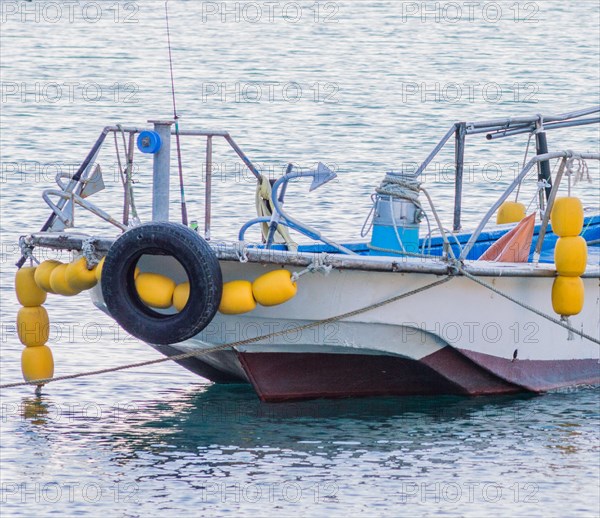 Moored fishing boat with yellow buoys and a tire on calm blue sea waters, in South Korea