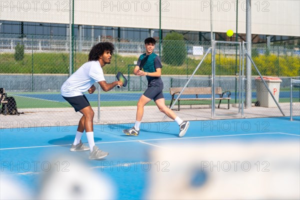 Multi-ethnic young sportive friends playing pickleball outdoors in a sunny day
