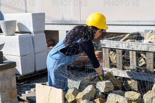 A construction worker in a yellow helmet is bending over as she works with stones