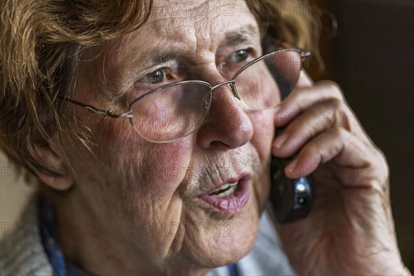 Senior citizen looks serious, frightened while talking on the phone in her living room, Cologne, North Rhine-Westphalia, Germany, Europe