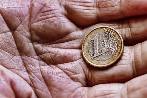 A euro coin in the wrinkled hand of a senior citizen, symbolising poverty and poverty in old age