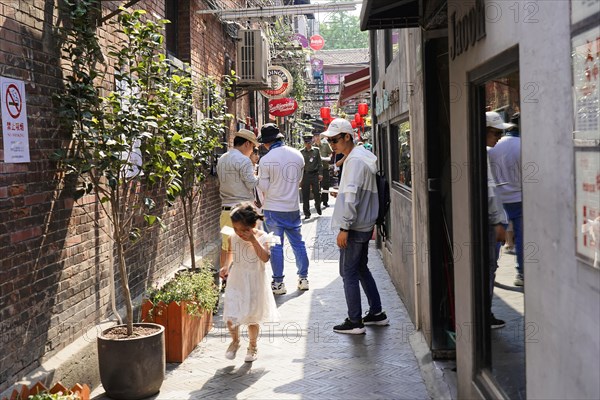 Strolling through the restored Tianzifang neighbourhood, people walking through a cobblestone alley with plants along the way, Shanghai, China, Asia