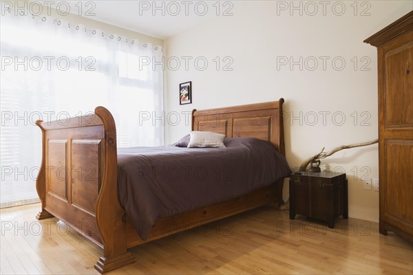 Antique wooden queen size sleigh bed in master bedroom inside a renovated ground floor apartment in an old residential cottage style home, Quebec, Canada, North America