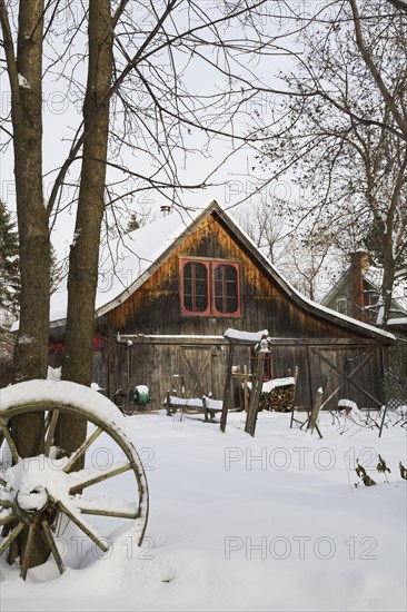Old wooden rustic barn with red trimmed windows framed by trees in backyard garden in winter, Quebec, Canada, North America