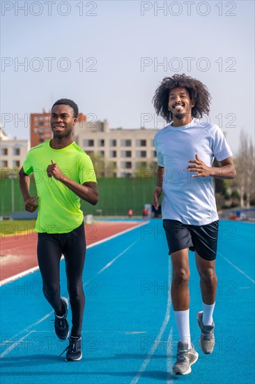 Vertical photo of two african american young ans sportive runners smiling while training together in an outdoor track