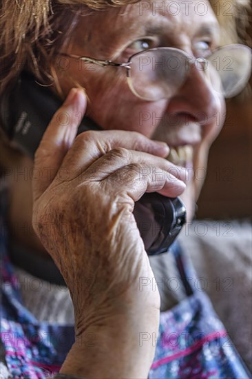 Laughing senior citizen with smock talking on the phone at home in her living room, Cologne, North Rhine-Westphalia, Germany, Europe