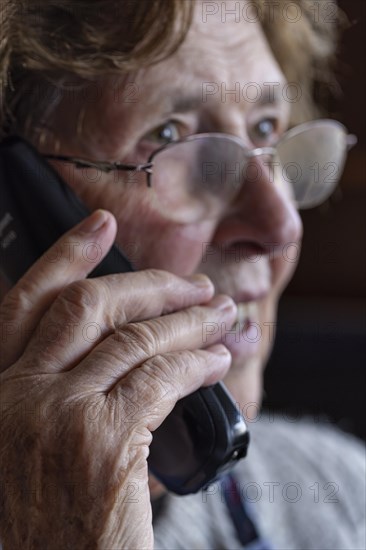 Senior citizen looks serious, frightened while talking on the phone in her living room, Cologne, North Rhine-Westphalia, Germany, Europe