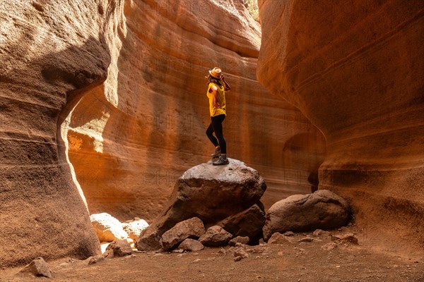 A person is standing on a rock in a canyon. The canyon is filled with rocks and dirt, and the person is wearing a yellow shirt