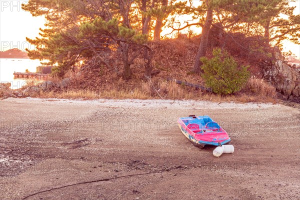 Small fiberglass boat beached on sandbar and tied to tree with sun setting in background in South Korea