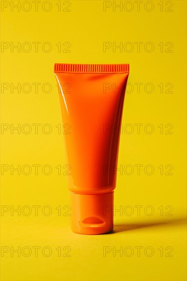 Orange sunscreen tube on yellow studio background. KI generiert, generiert, AI generated