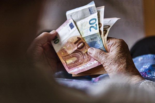 Senior citizen with wrinkled hands counts her money at home in her flat and holds banknotes in her hand, Cologne, North Rhine-Westphalia, Germany, Europe