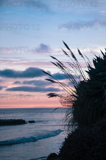 A beautiful sunset over the ocean with a beach in the background. The sky is filled with clouds, and the water is calm