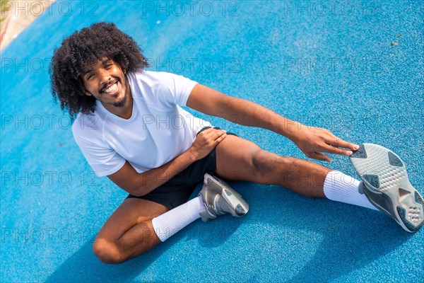 Sportive man with afro hairstyle warming up and stretching in an outdoor running track