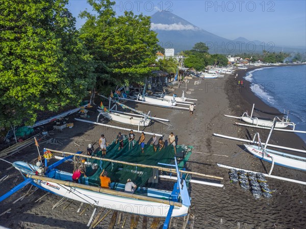 Fishermen loading fish from their outrigger boats in the morning on the black beach of Amed, Mount Agung in the background, Amed, Karangasem, Bali, Indonesia, Asia