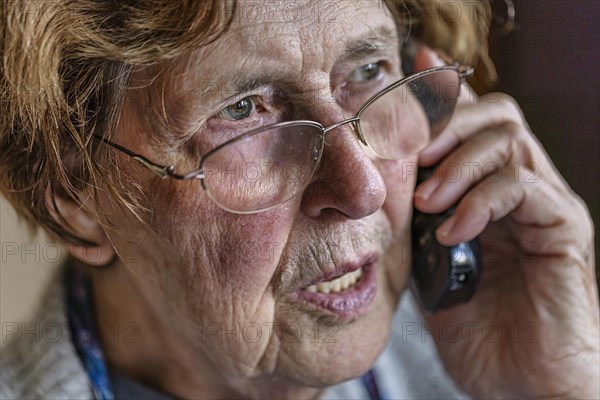 Senior citizen looks serious, frightened while talking on the phone in her living room, Cologne, North Rhine-Westphalia, Germany, Europe