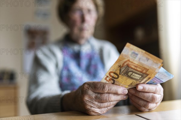 Senior citizen with wrinkled hands counts her money at home in her flat and holds banknotes in her hand, Cologne, North Rhine-Westphalia, Germany, Europe