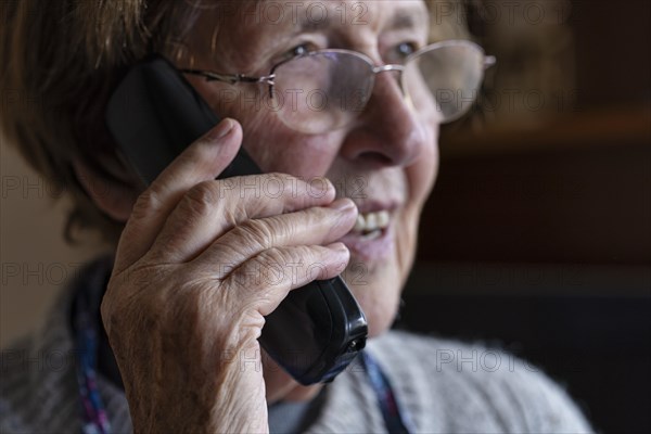 Laughing senior citizen with smock talking on the phone at home in her living room, Cologne, North Rhine-Westphalia, Germany, Europe