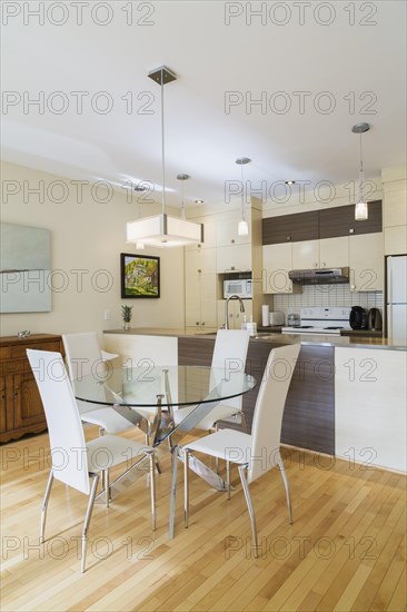 Dining room with round glass table, white leather high -back chairs and kitchen inside a renovated ground floor apartment in an old residential cottage style home, Quebec, Canada, North America