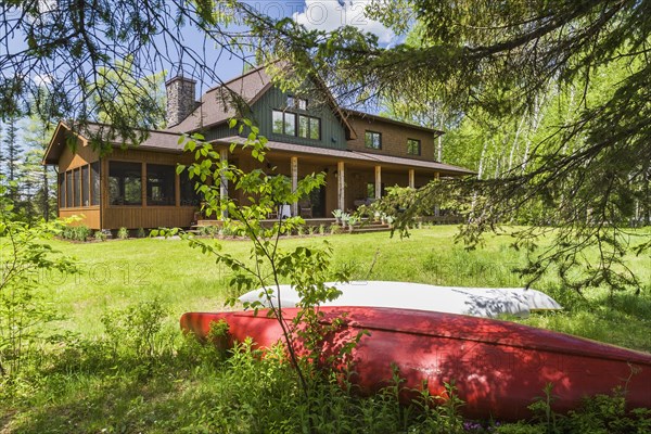 Rear view of brown and green stained spruce wood and cedar shingle siding LEED certified Country home with veranda in late spring, Quebec, Canada, North America