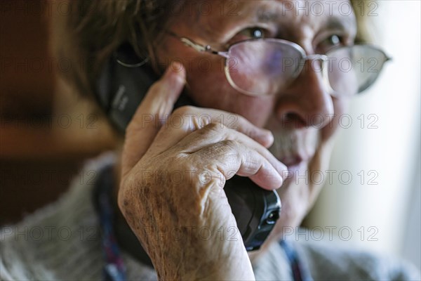 Senior citizen looks serious, frightened while talking on the phone in her living room, Cologne, North Rhine-Westphalia, Germany, Europe