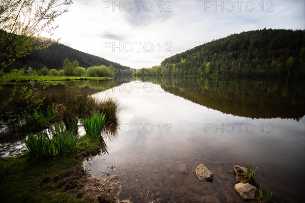 A lake in a landscape shot. A sunset and the natural surroundings are reflected in the water of the reservoir. Marbach reservoir, Odenwald, Hesse